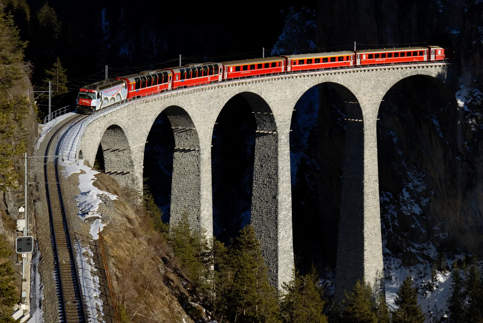 A red Swiss passenger train crossing the stone Landwasser Viaduct