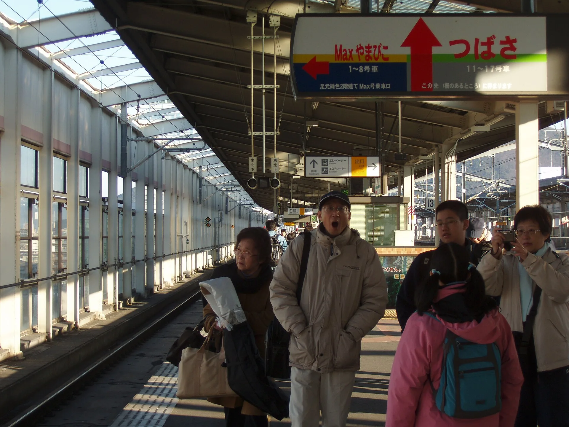 Passengers standing beneath boarding signs on a Japanese Shinkansen platform