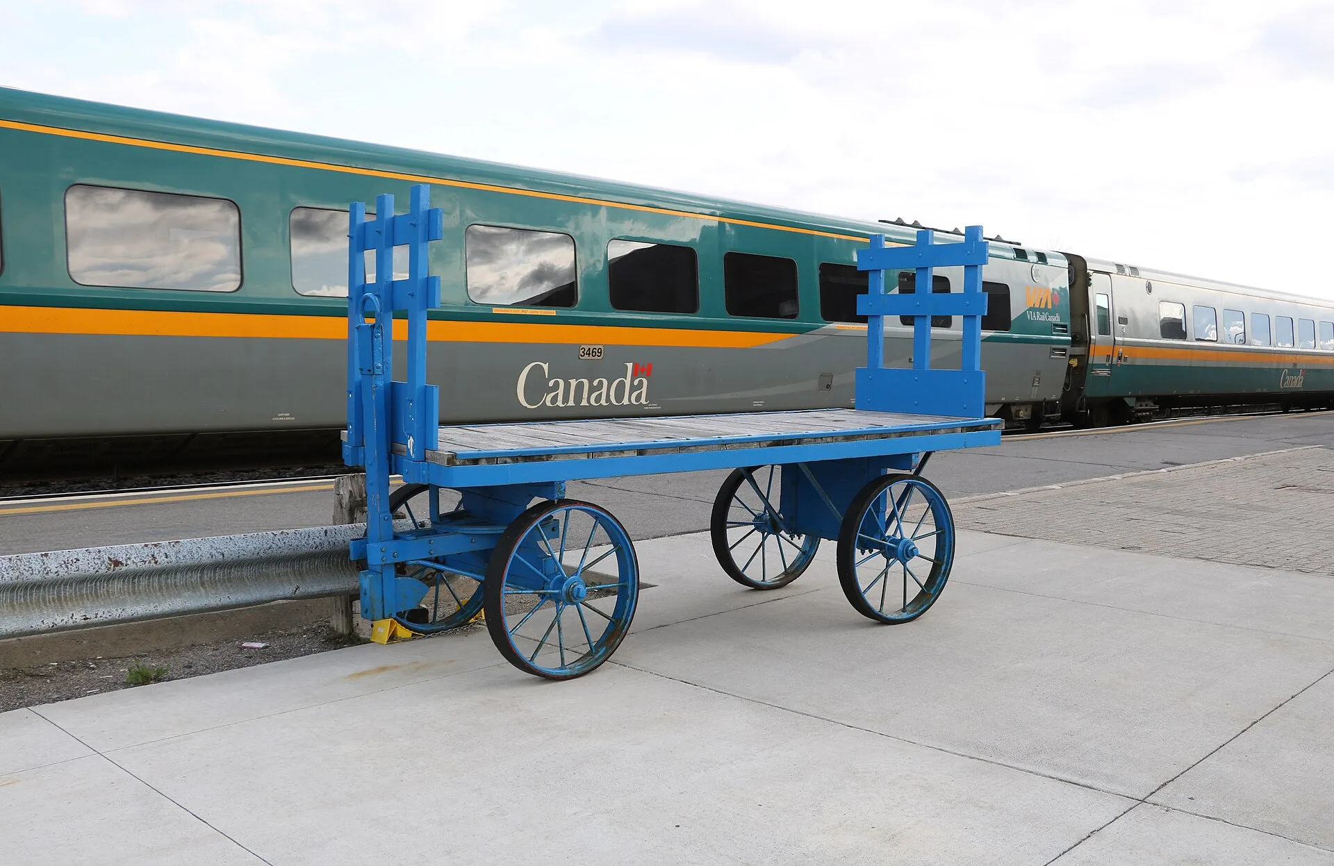 Empty blue luggage carts beside a VIA Rail passenger carriage